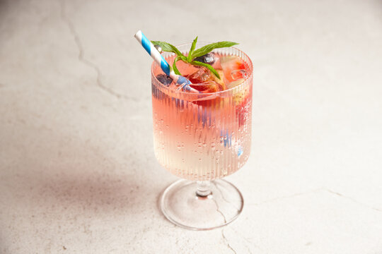 Close up shot of pink lemonade with white and blue striped straw and mixed berries