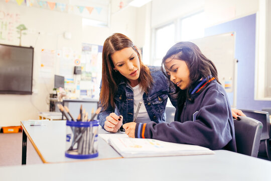 Aboriginal female school teacher sitting with her student in the classroom
