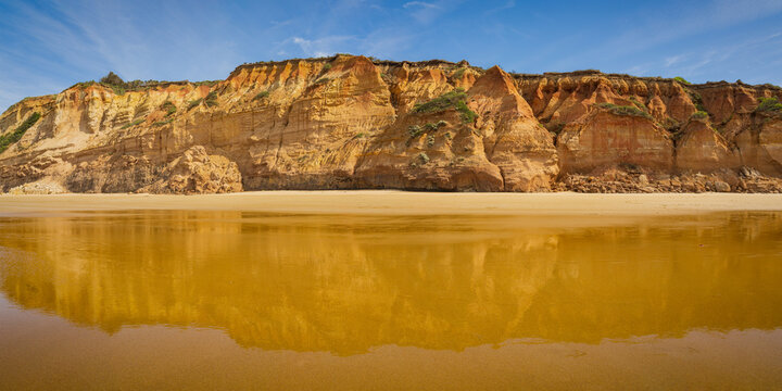 Low angled view of coastal sea cliffs reflected in wet sand on the beach below