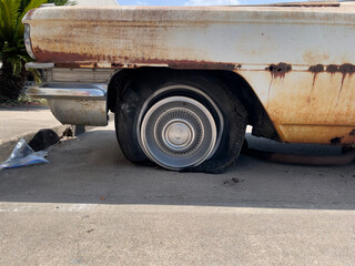 A rusty old car with a very flat tire.