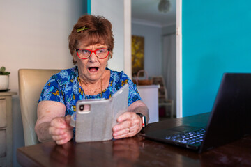 surprised older woman trying to use phone and laptop technology