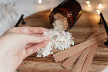 A woman 's hand holds in her hands flakes of white soy wax for making candles are scattered on a...