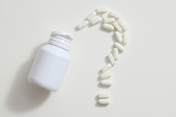 An unlabeled white bottle next to pills arranged in the shape of a question mark on a white background. Mockup for medication advertising.