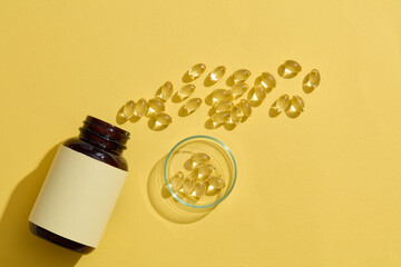 Against a yellow backdrop, an unlabeled medicine bottle, some scattered yellow soft capsules, and...