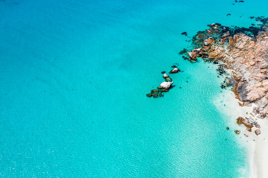 Aerial view of clear turquoise water, beach, and rocky point at Meelup Beach.