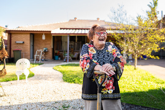 Happy senior woman outside in garden leaning on spade laughing