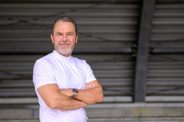 Side view of a man has his arms crossed and looks friendly at the camera