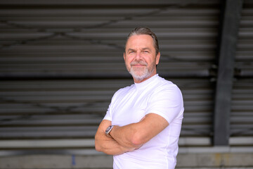 Side view of a man has his arms crossed and looks friendly at the camera