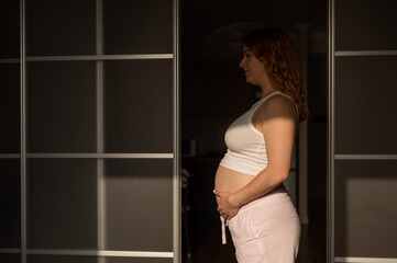 A pregnant woman in shorts and a crop top stands in profile between folding doors.