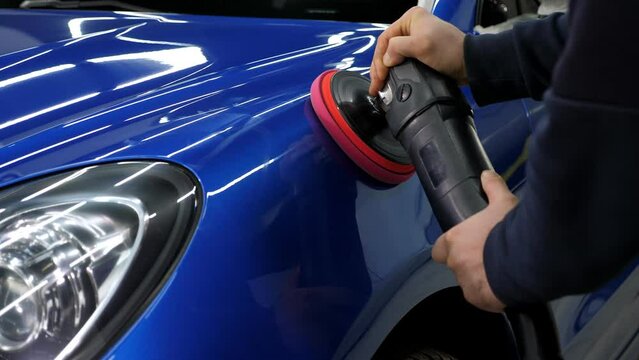 A man polishes a blue car with a car polishing machine at a car dealership. Car detailing and polishing concept. 