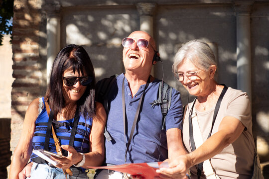 Joyful group of senior friends visiting Granada listening to information via audio guide. Elderly man and two women enjoying vacation and retirement in Europe