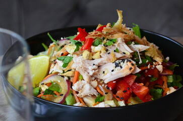 Salad with chicken, vegetables and sesame seeds in black bowl, close up view of asian chicken salad served in restaurant