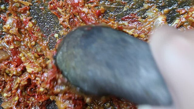 An asian hand pounding red chili, onion, garlic and tomato, with stone mortar and pestle. Process to make sambal, an Indonesian condiment food