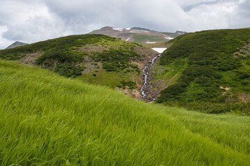 Summer mountain landscape. A stream on the side of a mountain. Travel, tourism and hiking on the Kamchatka Peninsula. Beautiful nature of Siberia and the Russian Far East. Kamchatka Territory, Russia.
