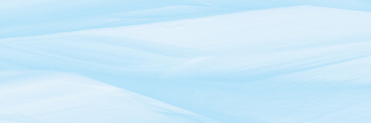 Wide panoramic winter background with snowy ground. Natural snow texture. Wind sculpted patterns on snow surface.