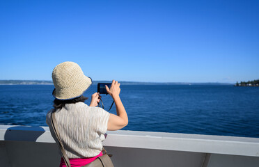 Woman taking photos using smartphone on the ferry at Elliott Bay. Seattle. Washington State.