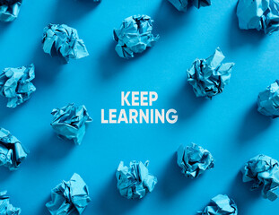 Keep learning message with crumpled blue paper balls on blue background. Continuous education and learning concept.