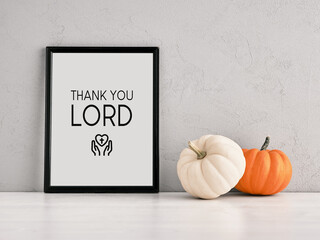 Pumpkins and a frame leaned on a gray wall with the quote Thank You Lord.