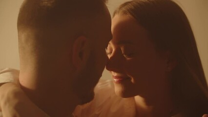 Young cheerful couple in love touch noses in bedroom. Two lovers bonding. Male touching his girlfriend nose while spending honeymoon together. Happy cute pair enjoying an intimate moment