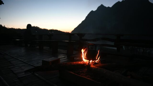 Old small kettle is heated on a bright bonfire on mountain in the rays of rising sun stunning morning during travel. Mountain Sunrise Adventure