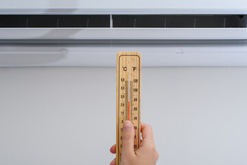 Kobieta trzyma termometr wewnętrzny na tle klimatyzatora  - obrazy, fototapety, plakaty