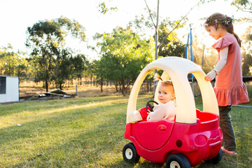 Two young aussie girls playing in rural backyard with plastic push car Cozy Coupe