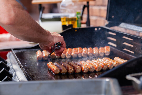 Australian person holding tongs turning greasy sausages on barbeque