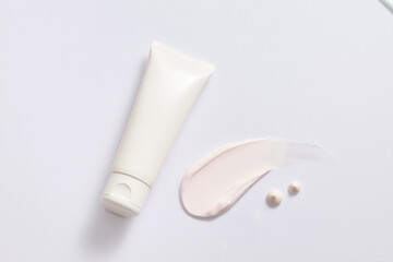 Top view of an unlabeled white cosmetic tube is placed next to a streak of pastel pink cream with a rich texture on a white background. Copy space for cosmetic advertising.