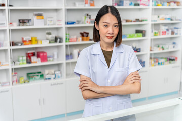 Happy beautiful asian female pharmacist wearing lab coat standing with arms crossed and looking at camera, She feels good, trustworthy and proud of his work in the pharmacy drugstore.