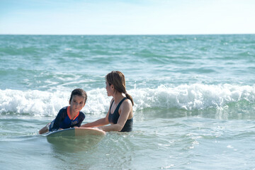 Obraz premium Little boy and mother waiting for big wave, mother teaches her son to surfing on wave, lifestyle activities, water sports