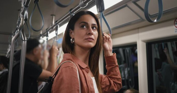 woman standing in subway side view in transport in a moving metro train holding the handles on top. Female standing in subway and waits for his stop. Nightlife in big city lifestyle concept.
