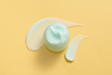 Looking from above, a jar of dense-textured moisturizer in a light blue against a yellow background. Scene for advertising various skincare creams or sleep masks.
