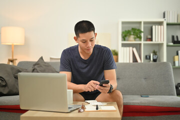 Handsome asian man calculating monthly expenses and managing household finances at home