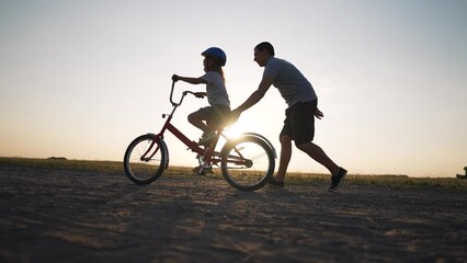 Happy family. Father teaches daughter to ride bike in park. Daughter riding bike for first time. Kid dream of traveling by bike. Girl is learning to ride a bike. Father helping hand to daughter