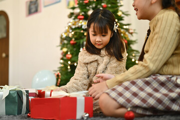 Fototapeta na wymiar Happy little girls opening Christmas gifts while enjoying holiday season together at home