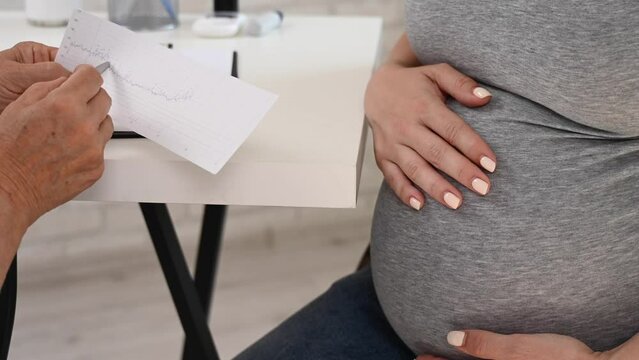 The doctor looks at the fetal cardiotocography. Pregnant woman at the reception at the gynecologist.