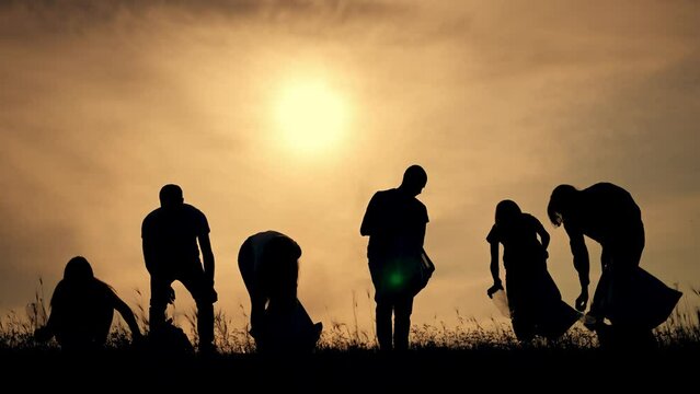 Teamwork.Silhouette of group of people clean up garbage at sunset in nature.Environmental pollution.Family cleaning plastic garbage in bag.People volunteers cleaning garbage in nature in summer park