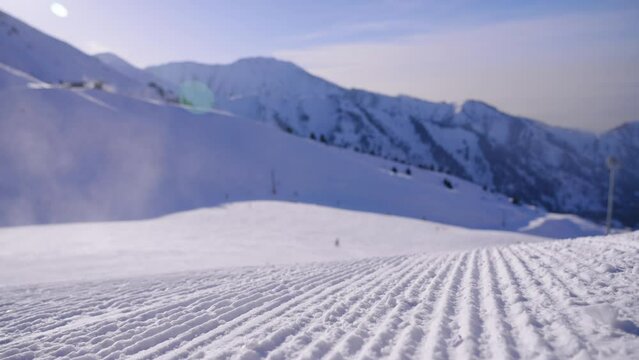 Close-up straight line rows of freshly prepared groomed ski slope piste. Prepared snowcat trail on a background of mountains. Snowcapped mountain downhill landscape at winter skiing resort.
