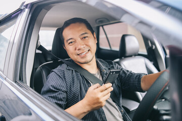 Portrait of friendly Asian online taxi driver looking at camera smiling and holding smart phone...