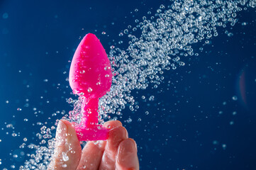 Woman washing pink anal plug under shower on blue background. 
