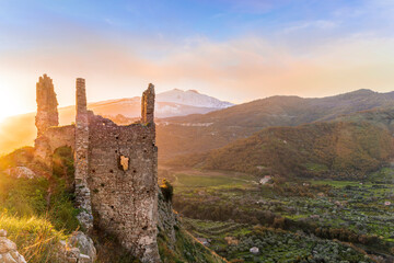 beautiful sunset or sunrise landscape of ancient ruins on a top of a hill with green mountains with white snow top on background