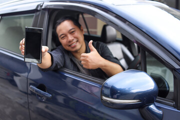 Male online taxi driver showing phone screen and thumb up while sitting in a car