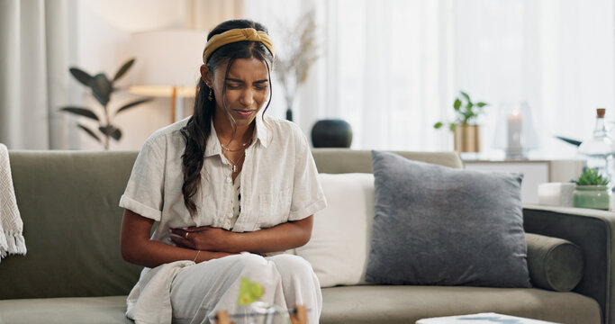 Stomach pain, woman and stress on couch at home with abdomen problem and constipation from virus. Sick person, menstruation and bloated belly ache from colon health issue and cramps in a living room