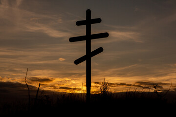 Cross on top of a hill against a blue sky with white clouds. Silhouette of a cross in the field at sunset with dramatic sky.