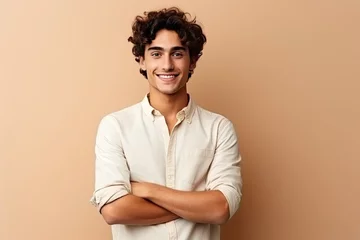 Tuinposter Portrait of a handsome young man with curly hair smiling at camera isolated over beige background, Happy young man. Portrait of handsome young man in casual shirt keeping arms crossed, AI Generated © Iftikhar alam