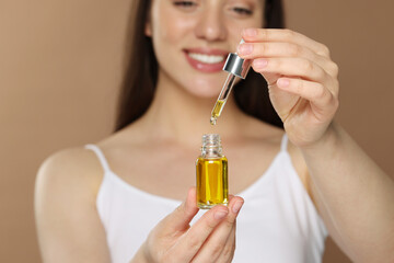 Fototapeta premium Woman with essential oil on brown background, selective focus