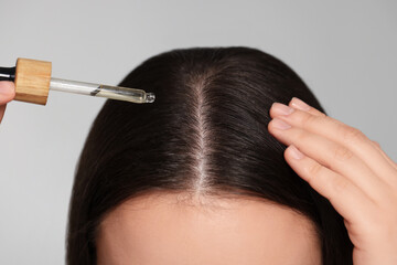 Woman applying essential oil onto hair on grey background, closeup