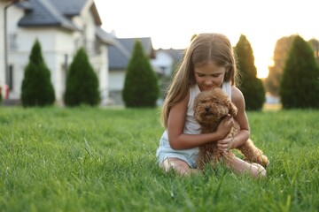 Beautiful girl with cute Maltipoo dog on green lawn in backyard