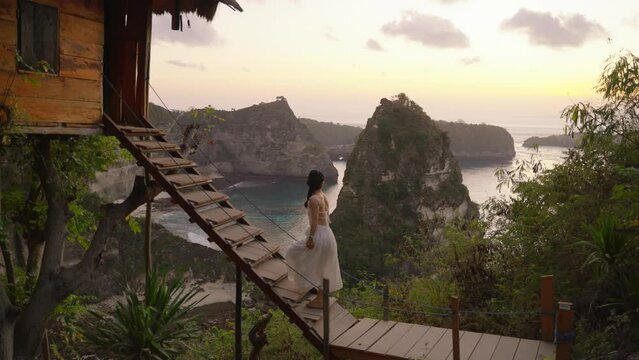 Nusa penida, Bali, indonesia, 4K video of woman white dress walking of tree house and looking at Atuh beach on tree house, Nusa Penida island at sunrise. Popular travel destination on Bali, indonesia.