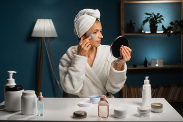 Attractive Hispanic 35 years old woman wears bathrobe and towel in bedroom applying patches,...